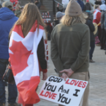 两个白色抗议者，一个穿着加拿大国旗，另一个拿着一个标志，说“上帝爱你，我爱你”。
