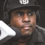 一个戴着黑色棒球帽和耳机的黑人站在麦克风前