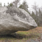 a large boulder that rocks in a field near a forest