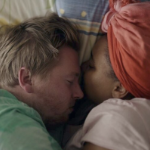 A white man and a Black woman snuggle in bed