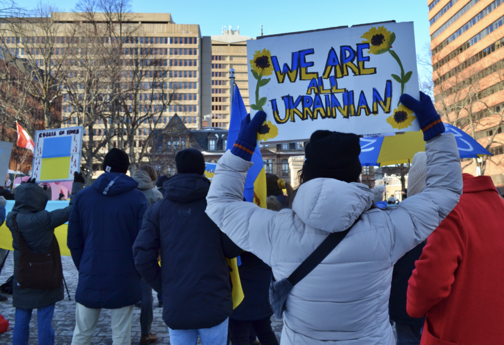 A woman holds aloft a sign with daisies on it that says 