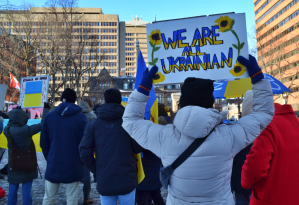 一名妇女高举着一个雏菊牌子，上面写着“我们都是乌克兰人”。