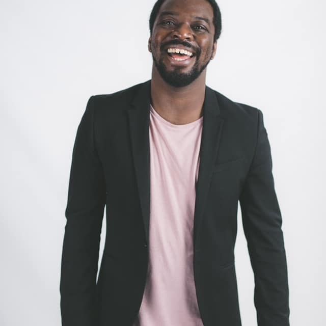 面带微笑的留着胡子的黑人，穿着浅色t恤外搭一件休闲的深色夹克