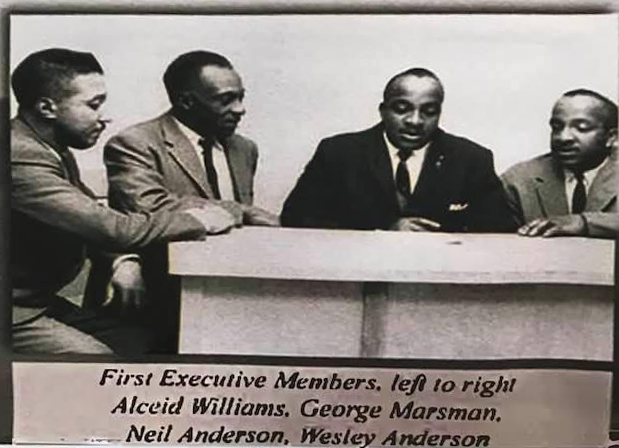 黑白的老照片，四个穿着西装的黑人坐在一张桌子旁