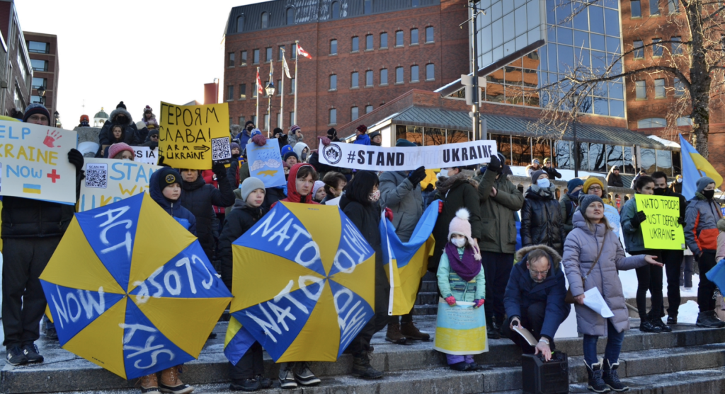 People holding colourful signs supporting Ukraine and condemning Russia stand on the steps at Grand Parade.