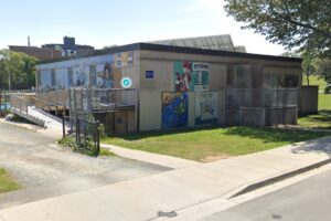 在一幅颗粒状的图片中可以看到一座小砖房，底部写着谷歌。这是一个阳光明媚的日子，在建筑的背面可以看到太阳能电池板，背对着镜头。