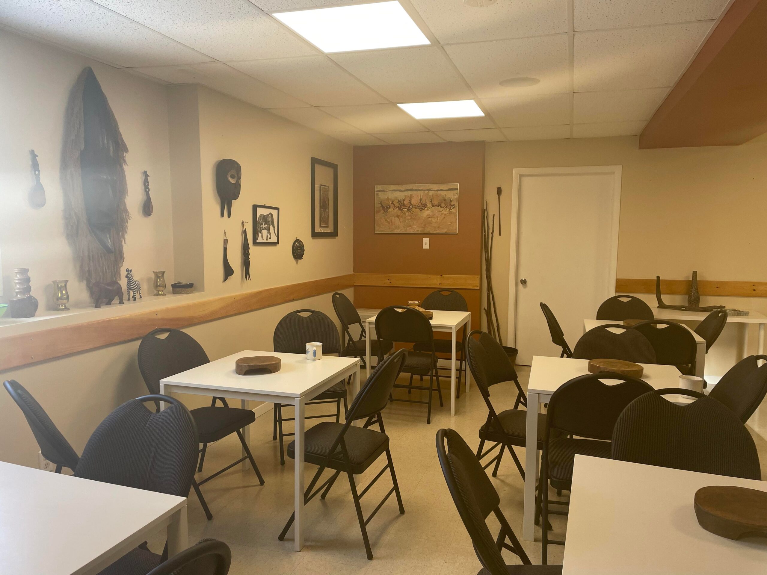 有白色桌子和黑色椅子的咖啡馆。米色的墙上挂着非洲艺术品