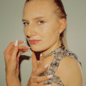 有长的金发的一名年轻白人妇女，湿和被光滑的后面，戴着顶部由珠宝肩带和长的白色指甲。