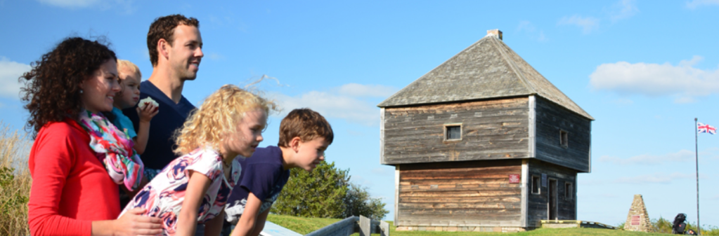 一个家庭，包括母亲、父亲和三个年幼的孩子站在一个小木制堡垒外，背景是飘扬的英国国旗。