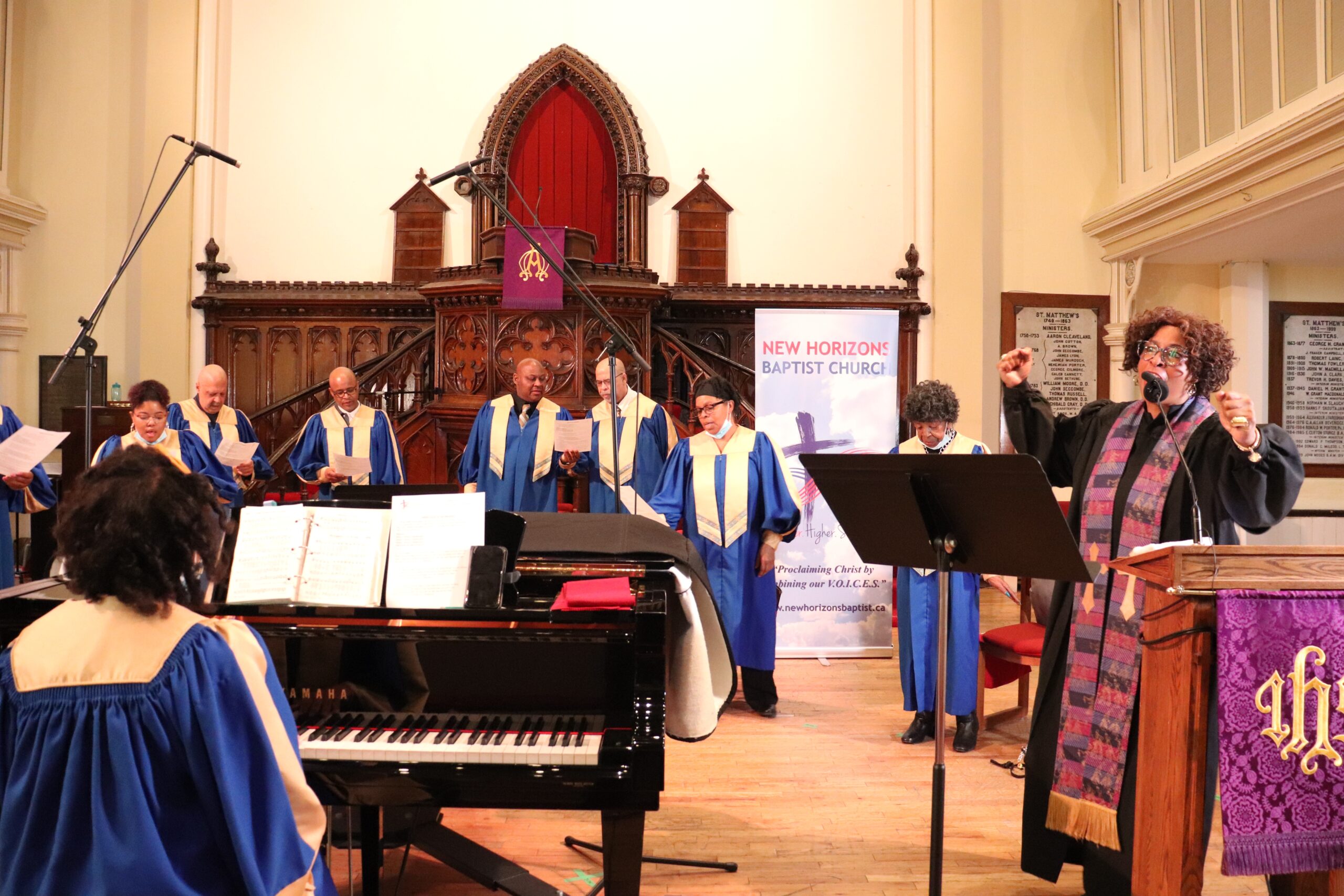 Black female pastor in Black robe leads an all-Black church choir in blue robes