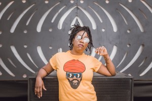 一个年轻的黑人妇女，戴着墨镜，穿着浅橙色的t恤