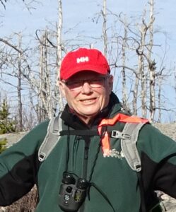 大卫·帕特里昆在树林里的照片，戴着一顶红色的棒球帽，穿着一件绿色的夹克，脖子上挂着双筒望远镜。(贡献)