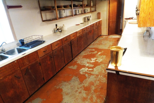 一个老旧的厨房，生锈的地板，旧的深色木橱柜，还有一个蓝色的平底锅。