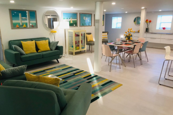 一个装饰有绿色沙发、黄色和绿色地毯、餐桌和黄色橱柜的空间。墙上有艺术品。