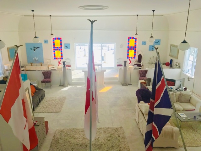 一个翻新的教堂避难所漆成白色，前景是旗帜，白色地板，红色，蓝色和黄色的彩色玻璃窗。