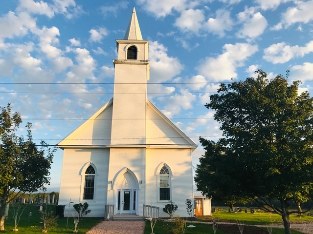 蓝天白云下的白色教堂尖顶。教堂旁边是一座墓地