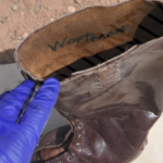 一只戴着蓝色乳胶手套的手摸着皇家骑警的棕色皮靴上面用黑色记号笔写着凶手的名字