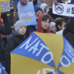 在抗议活动中，孩子们举着一把蓝黄相间的雨伞，上面写着“北约”