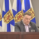 市长约翰·萨维奇在几面新斯科舍省旗帜前的一张桌子前