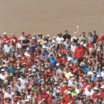 一大群人站在海滨，身后是一片泥泞的水域