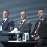 Three white men in dark suits sit at a table