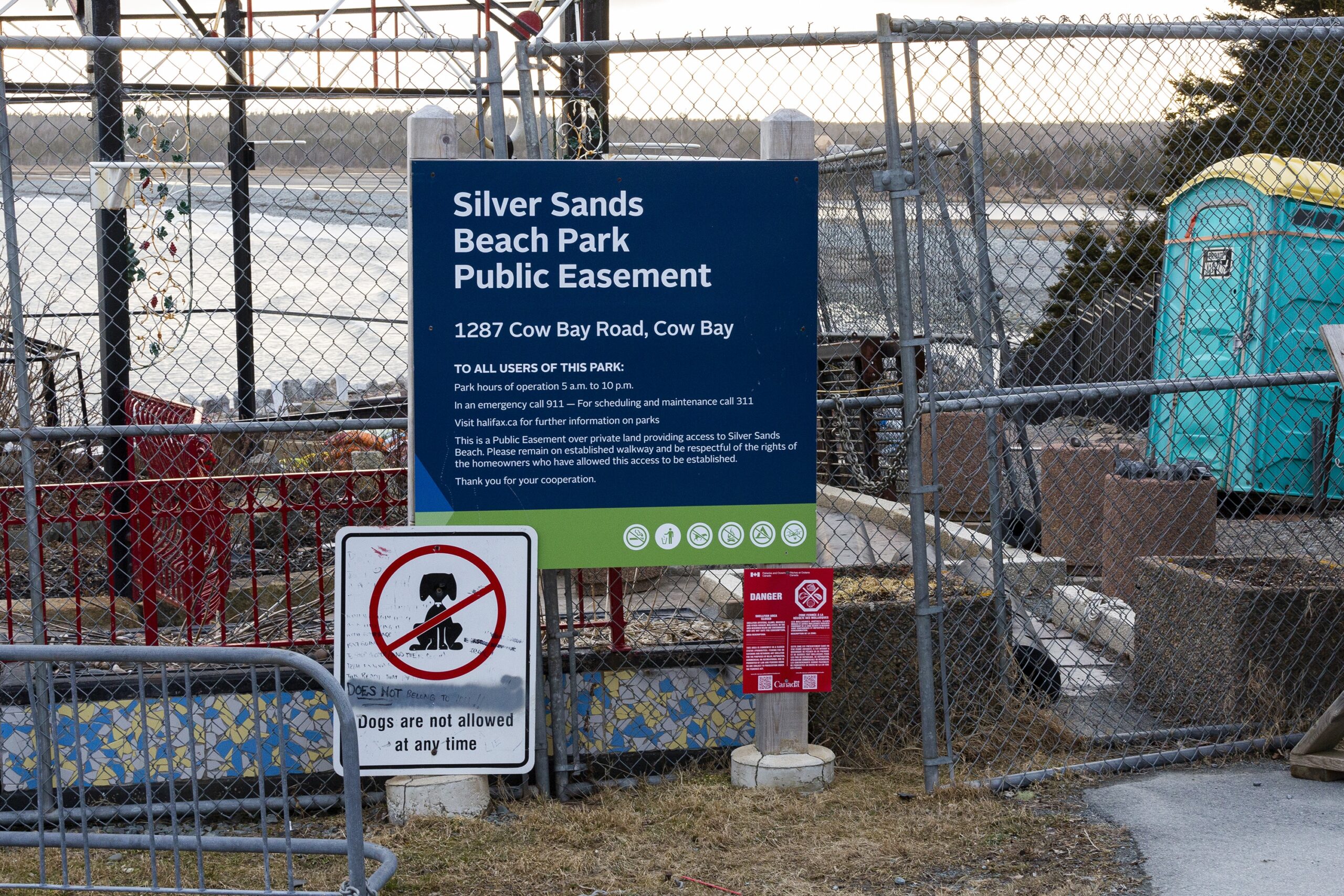 杂乱的标识和栅栏随处可见。最大的标志是蓝绿相间的，上面用白字写着公园的名称和地址，牛湾路1287号。下面是一个标记，上面划掉了狗的名字:“现在任何时候都可以带狗。”中间有一个移动厕所，后面是海滩。