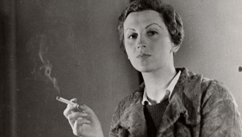 黑白照片，一个年轻的白人女子留着短发，拿着一支烟