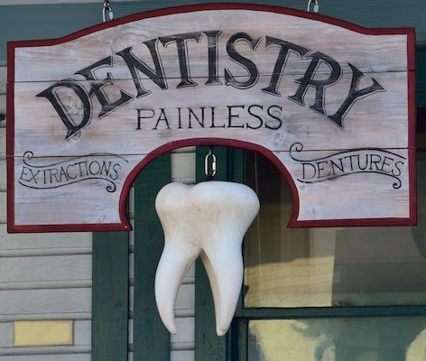 一个写着“牙科，无痛”的木牌，上面挂着一颗大臼齿