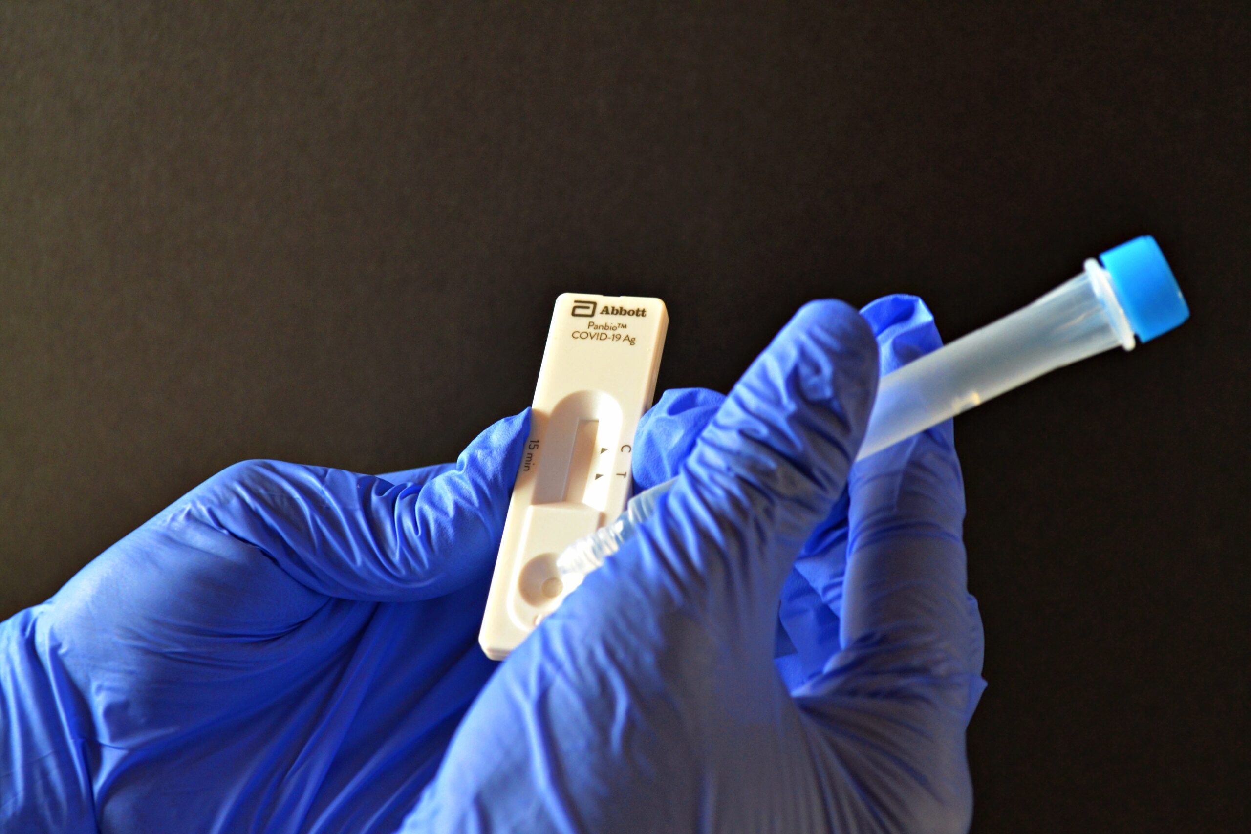戴蓝色医用手套的人一手拿着COVID-19快速测试仪，右手往测试仪的井里滴一滴液体。