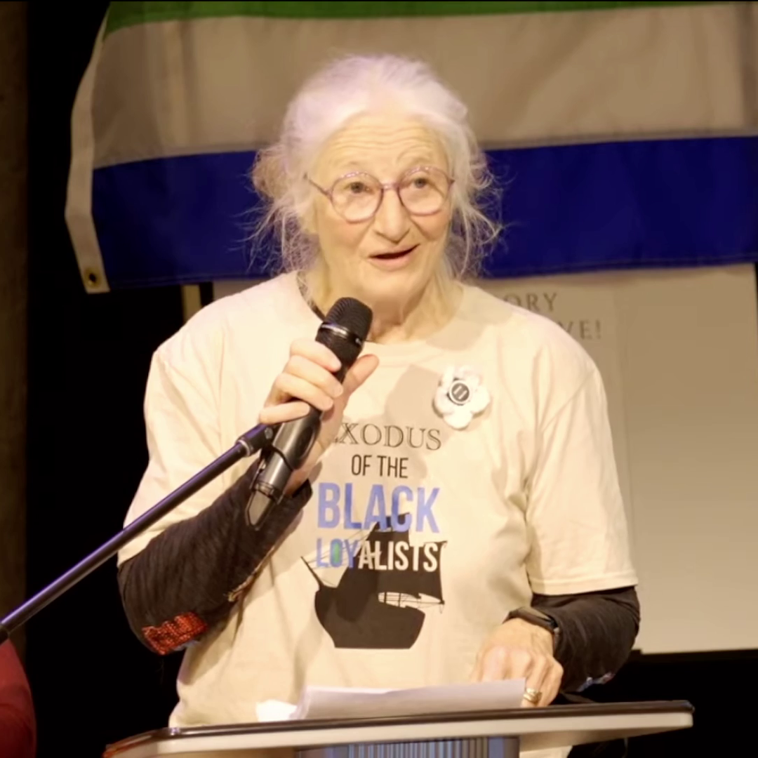 戴眼镜、白发的白人女士在讲台上讲话。