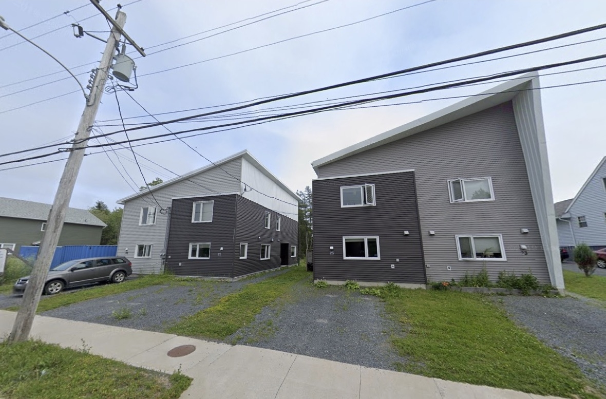 在阳光明媚的日子里可以看到两所房子。这些房子是三种深浅不一的灰色，斜拱向上和向右突出。前面的砾石车道上有一些绿色的草地，还有一条混凝土人行道，头顶上有电线。