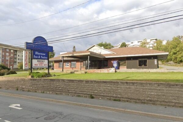 阴天可以看到一家昏暗的汽车旅馆。在前面的招牌上，上面用褪了色的字母写着霍华德·约翰逊。下面是Bluenose Inn & Suites。下面是几个可拆卸的字母:每月1000美元和一个电话号码，然后是旅馆的网站thebluenoseinn.com。