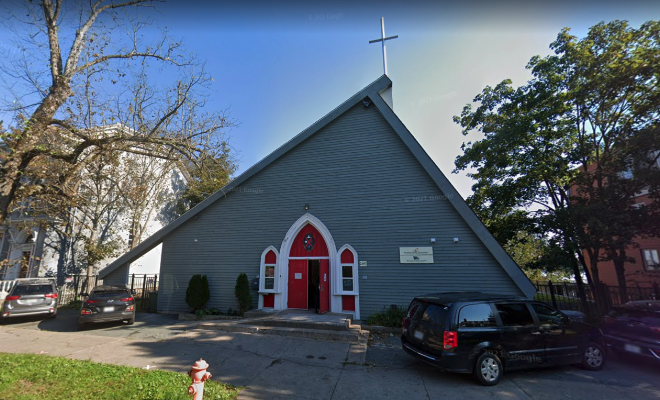 Exterior of the Brunswick Street Mission, which is an A-frame grey wood building with red arched doors.