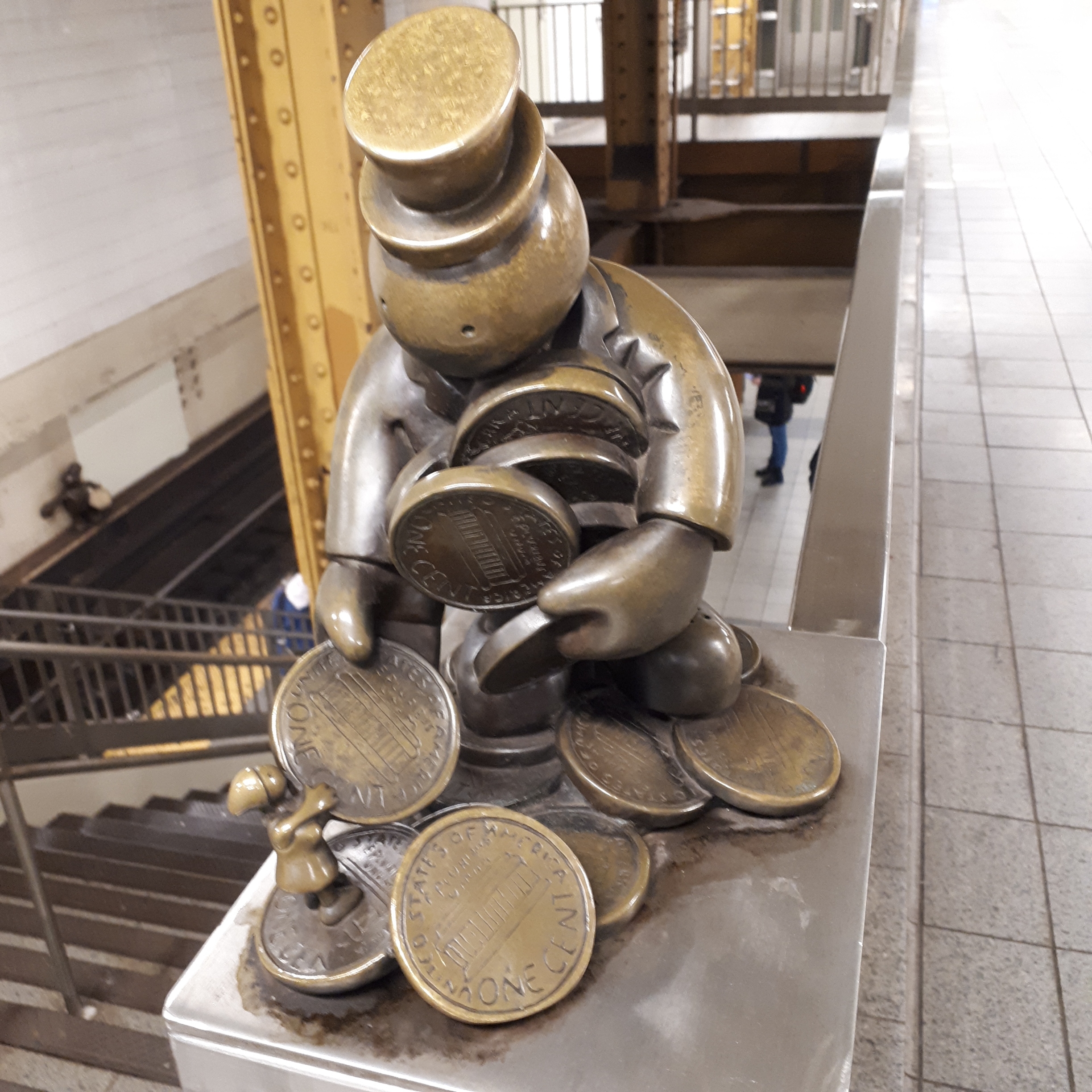 一个戴礼帽、抱着一大把硬币的男人的铜像，正从一个小小的人物手里拿另一枚硬币。