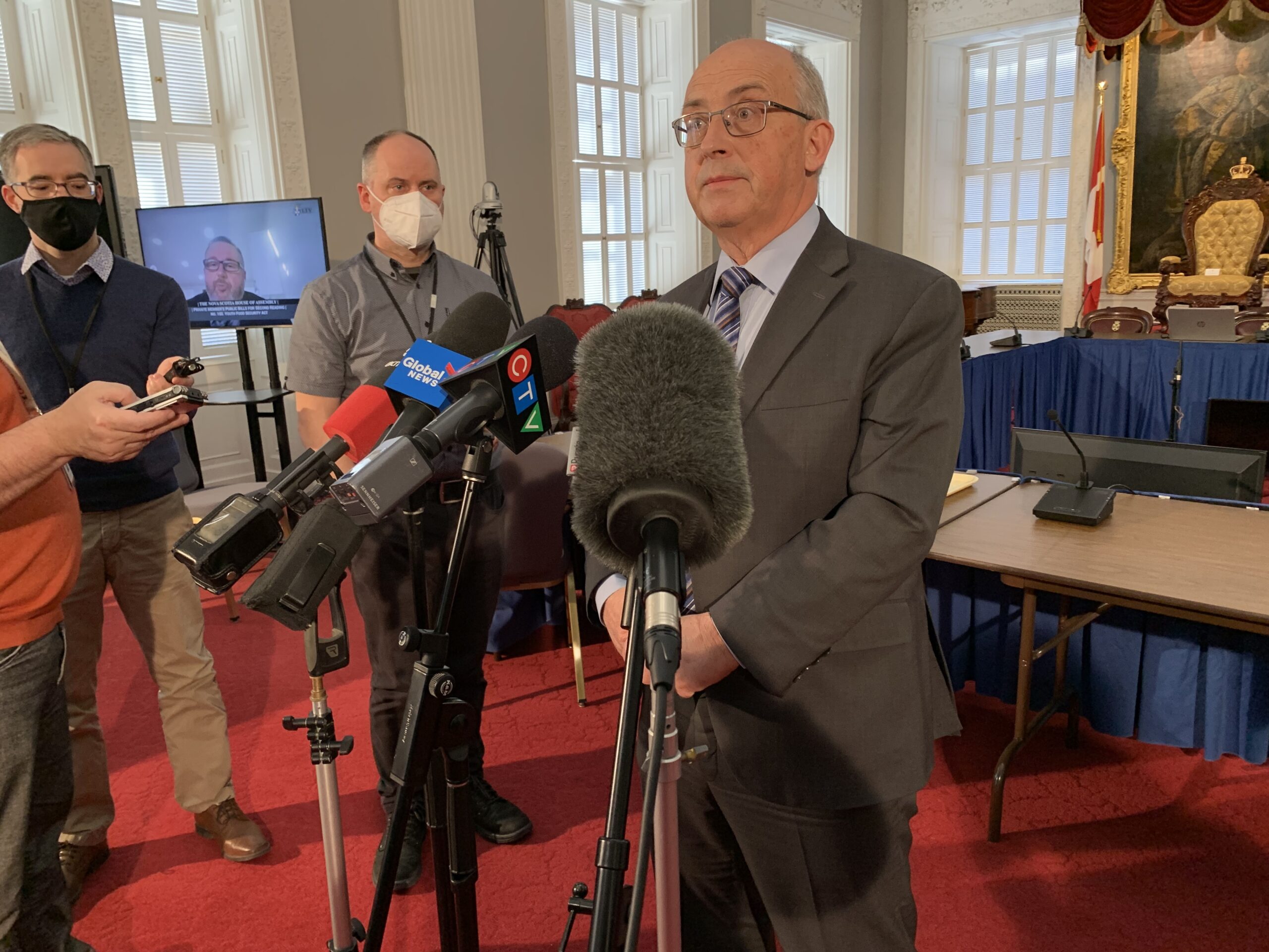 A man with glasses standing at a microphone at a press scrum in the legislature