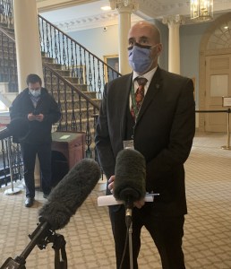 一名身穿西装、戴着面具的秃头男子站在麦克风前