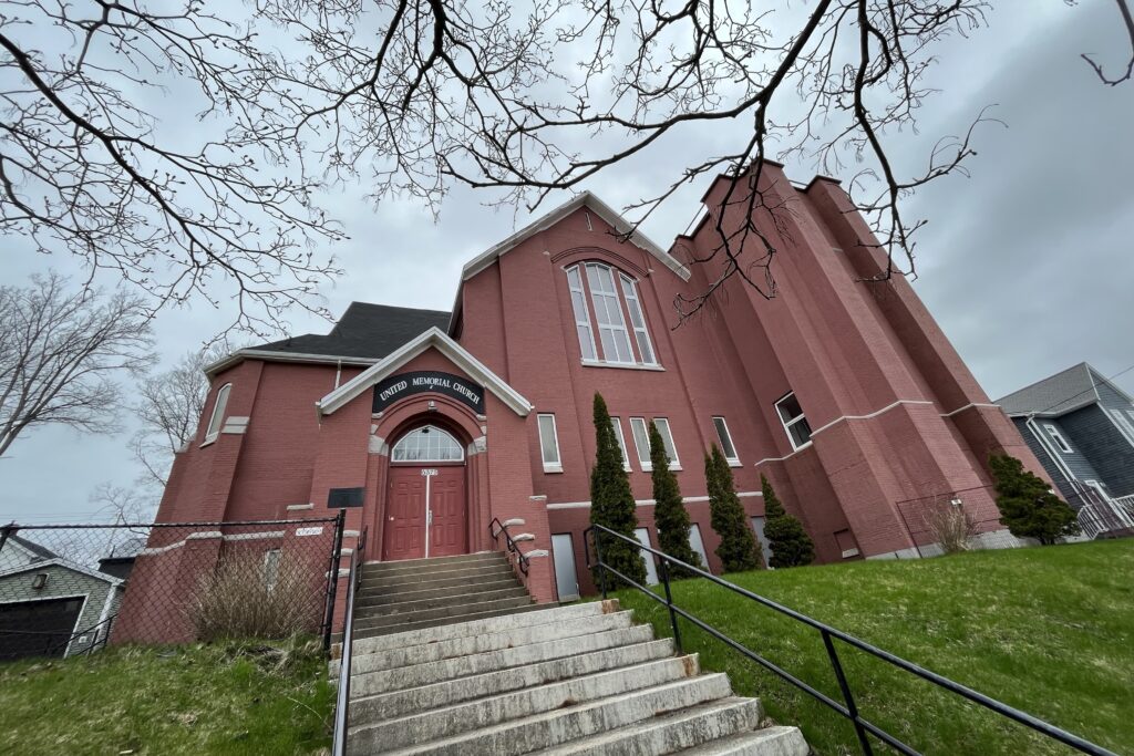 大的红砖建筑出现在灰色的一天。The photo is taken from a low, wide angle, and tree branches extend ominously from the top of the frame. Above the door to the building, the words 