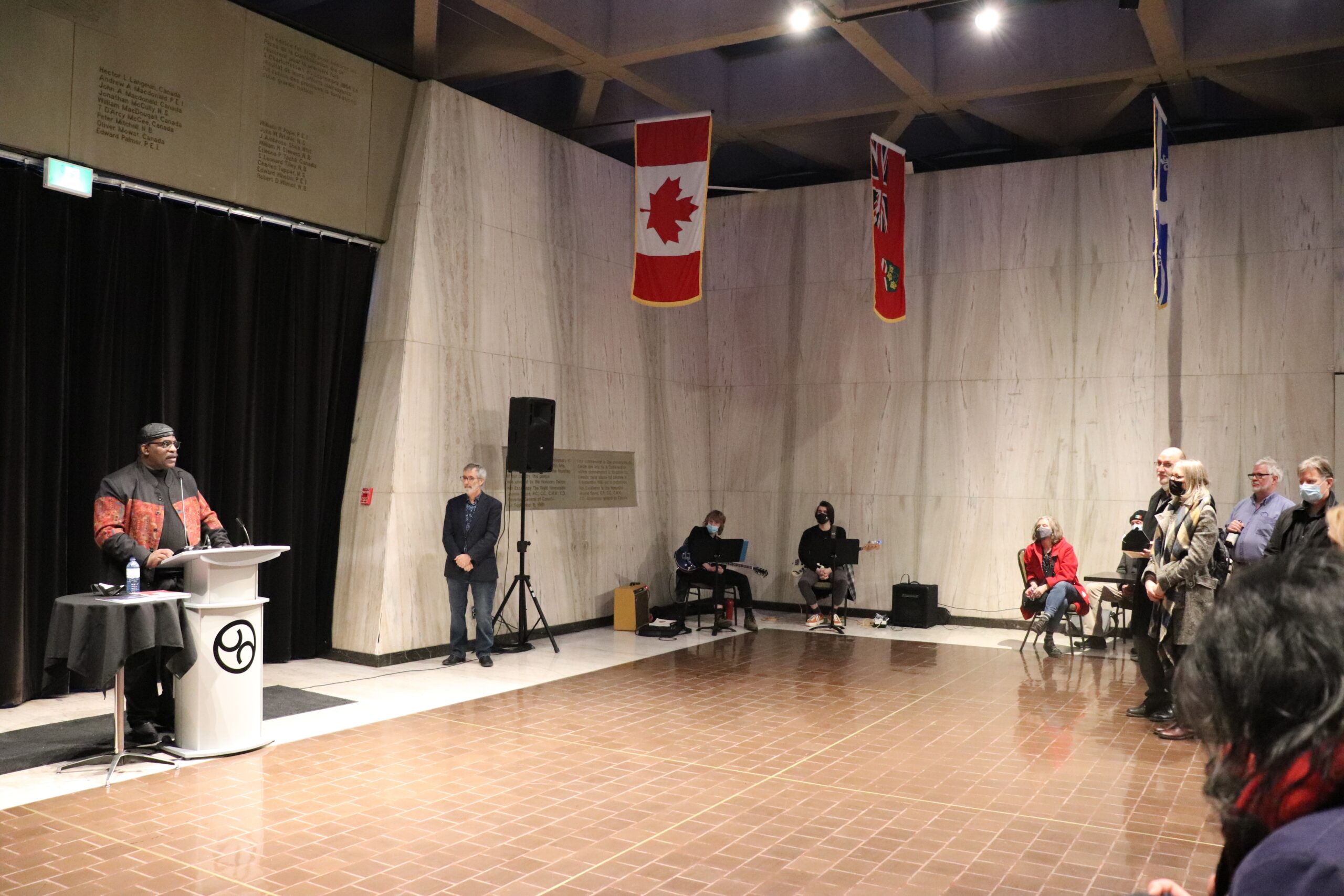 在一个水泥墙的大房间里，大卫·伍兹在讲台上向观众发表讲话。