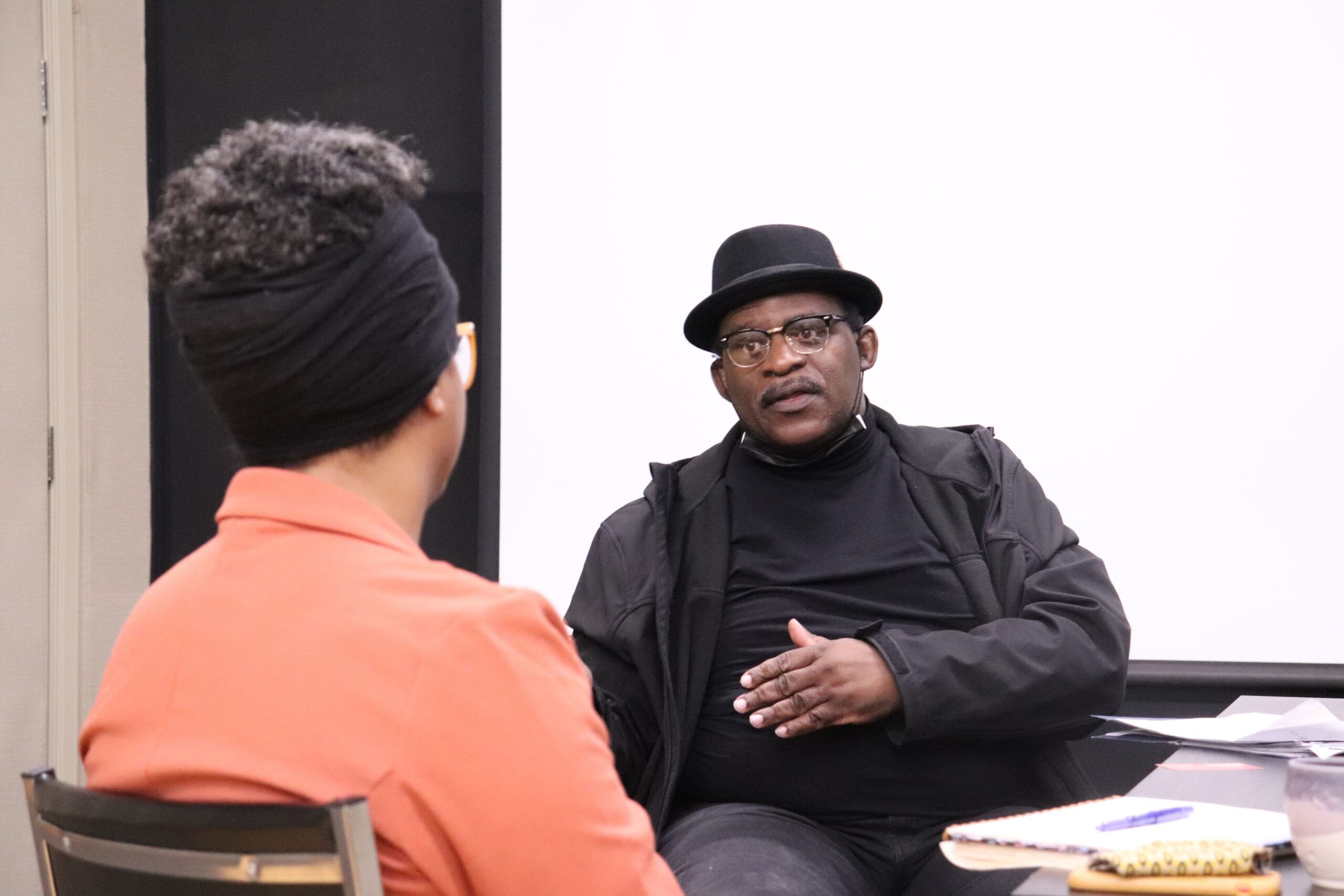 Black man in Black fedora, black glasses, black shirt, and black jacket.