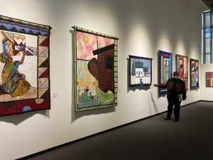 几张描绘非洲新斯科舍省社区图像的被子并排挂在一面白墙上，大卫·伍兹(David Woods)带领游客参观