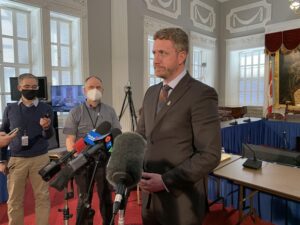 伊恩·兰金穿着西装，打着领带，看起来很严肃，他在议会大厦与记者交谈。