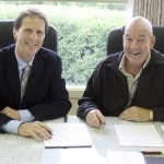 两个面带微笑的白人坐在桌子前，面前放着笔记本和笔。