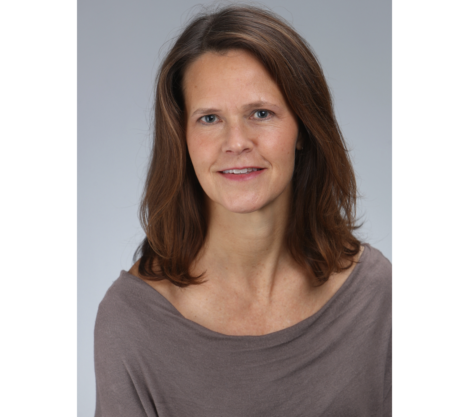 A smiling woman with shoulder length brown hair wearing a brown shirt smiles against a grey background.