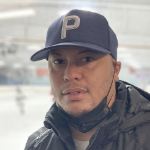 一名黑人男子戴着黑色棒球帽，戴着面具，在曲棍球场内