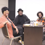 一个黑人妇女和两个黑人男子坐在一张桌子旁