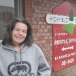 一个身穿灰色卫衣的白人妇女站在一座砖房前