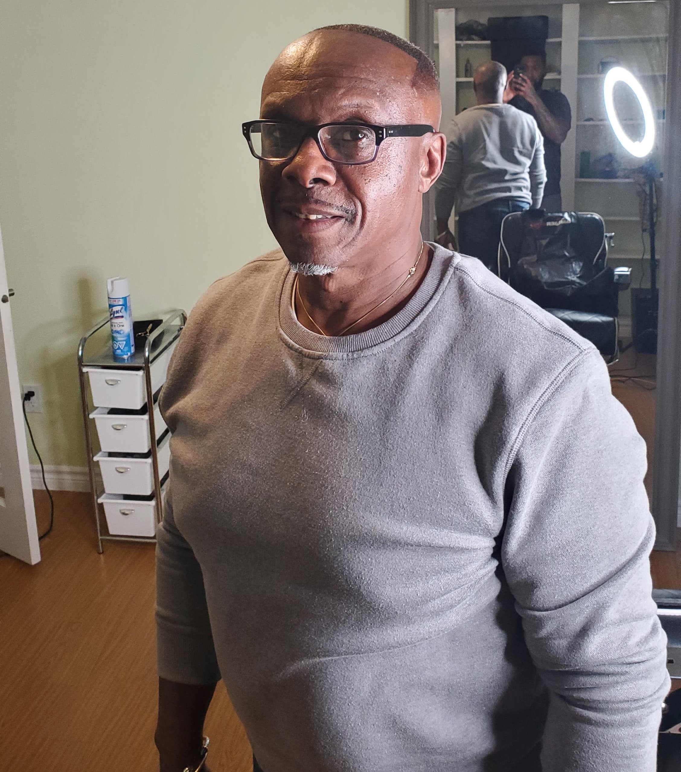 戴着黑眼镜、穿着灰色毛衣的黑人对着镜头微笑