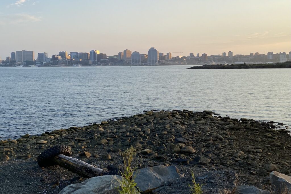 哈利法克斯城的天际线在达特茅斯的日落时看到。在前景中，有一个带有原木和旧轮胎的岩石露头。国王码头码头中的中间地面上还有另一个岩石露头。