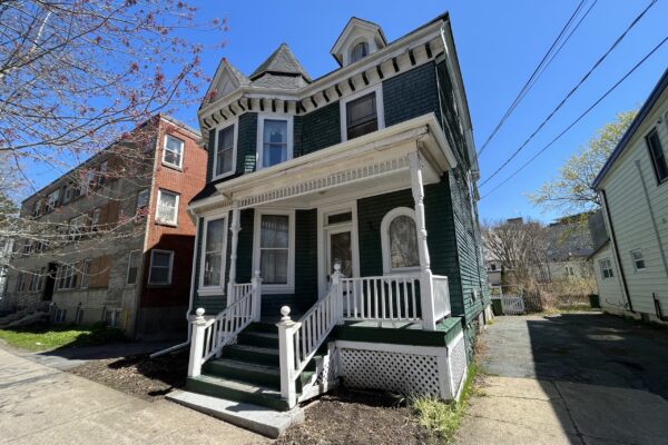 在一个阳光明媚的日子里可以看到一座老房子。它是森林绿色的，有白色的装饰和雪松木瓦。有一个复杂的屋顶线，有一个天窗，在炮塔上有一个阶梯式的山峰。