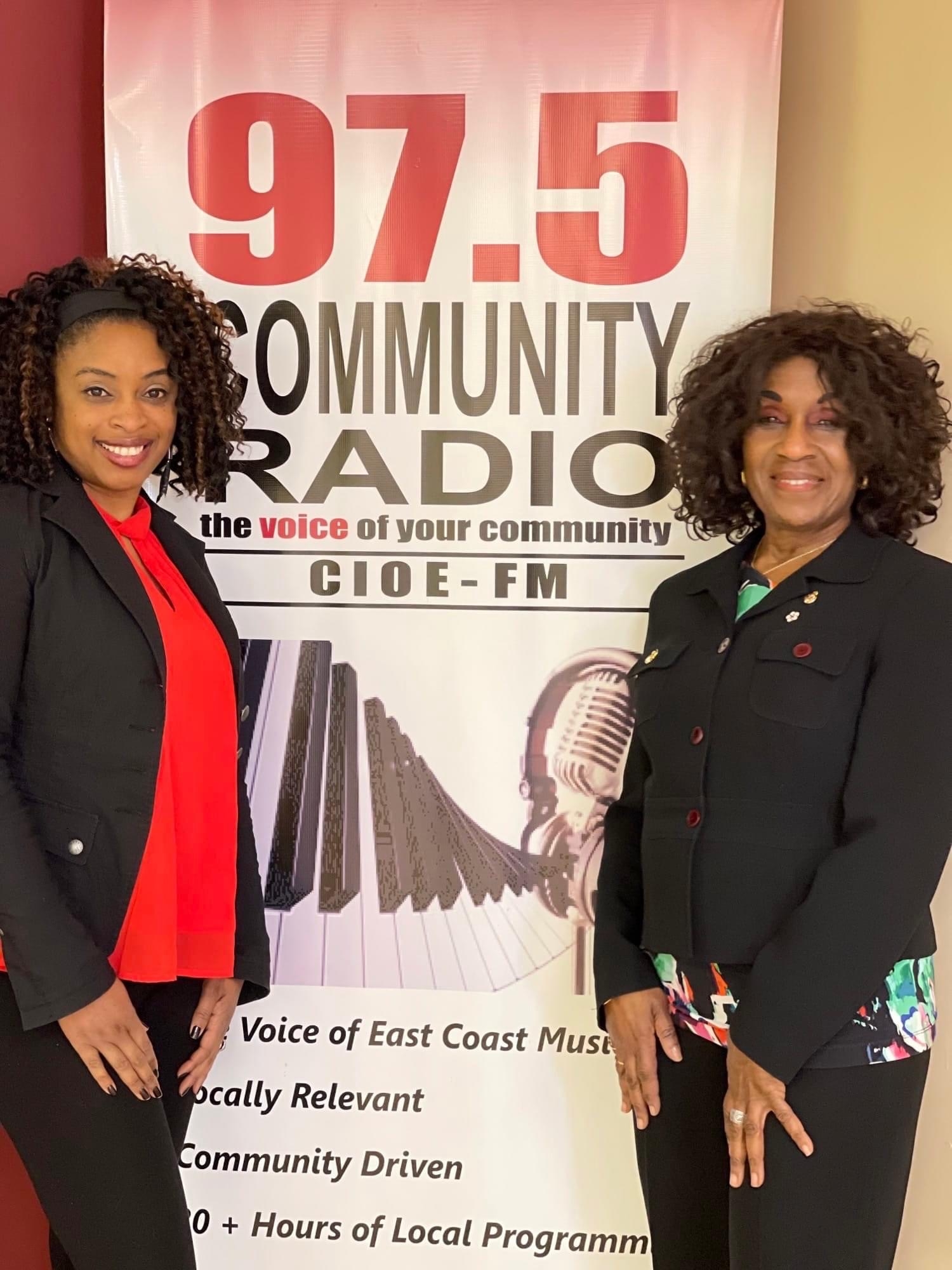 Two Black ladies pose in front af a radio station promotional poster